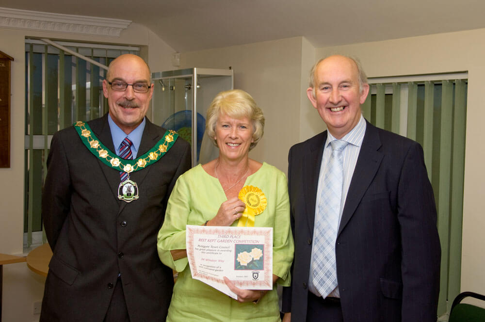 A lady receives a winners rosette and certificate for her garden